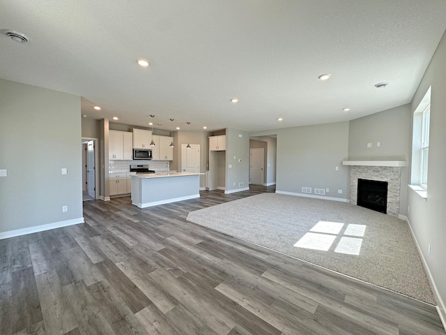 unfurnished living room with visible vents, baseboards, dark wood finished floors, a stone fireplace, and recessed lighting