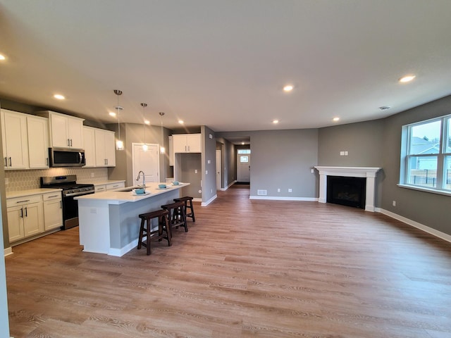 kitchen with a center island with sink, a sink, white cabinets, appliances with stainless steel finishes, and light wood-type flooring