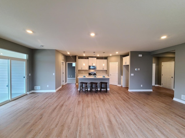 unfurnished living room featuring visible vents, baseboards, and light wood-type flooring