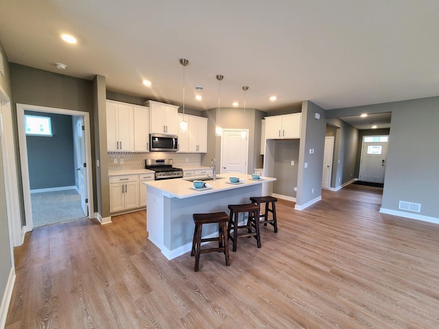 kitchen with visible vents, a kitchen island with sink, white cabinetry, appliances with stainless steel finishes, and light wood finished floors