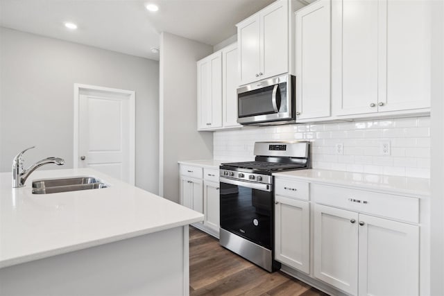 kitchen featuring dark wood finished floors, a sink, decorative backsplash, light countertops, and appliances with stainless steel finishes