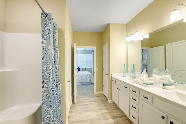 ensuite bathroom with a sink, connected bathroom, wood finished floors, and double vanity