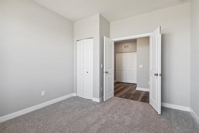 unfurnished bedroom featuring visible vents, dark colored carpet, a closet, and baseboards