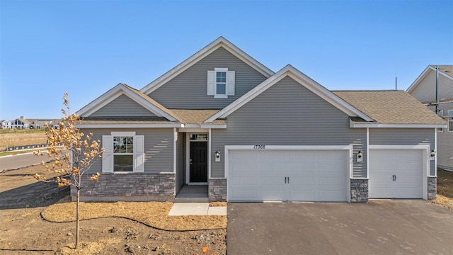 view of front facade with a garage, stone siding, driveway, and a shingled roof