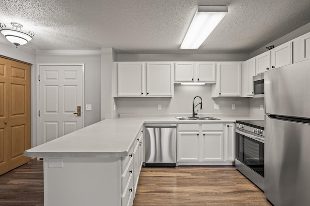 kitchen with dark wood-type flooring, a sink, appliances with stainless steel finishes, a peninsula, and light countertops