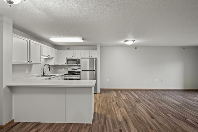 kitchen featuring dark wood-type flooring, light countertops, appliances with stainless steel finishes, a peninsula, and a sink