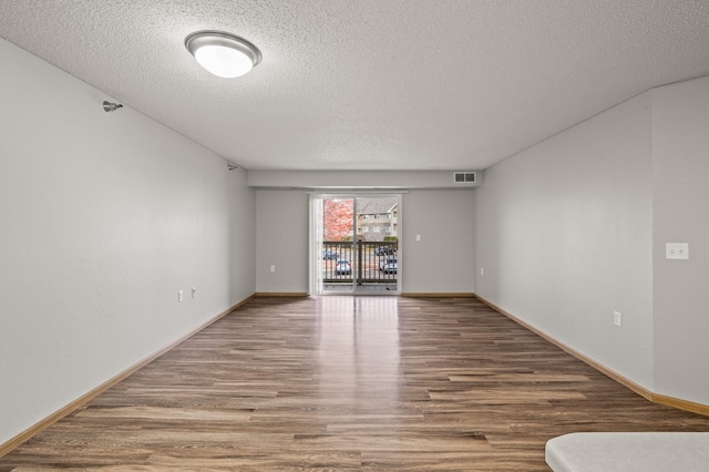 spare room with visible vents, baseboards, a textured ceiling, and wood finished floors