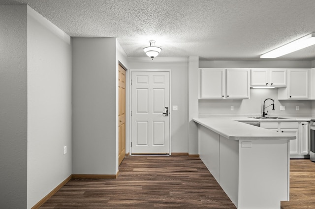 kitchen with dark wood-style floors, a peninsula, a sink, light countertops, and white cabinetry