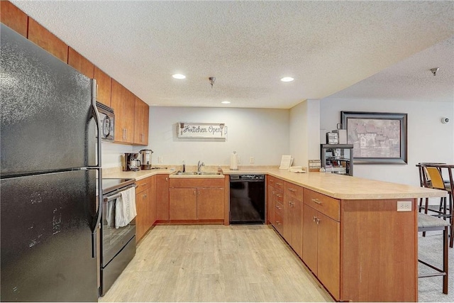 kitchen featuring black appliances, a breakfast bar, a sink, a peninsula, and light countertops