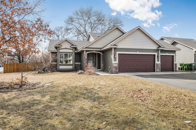 craftsman-style house with fence, a front yard, a garage, stone siding, and driveway