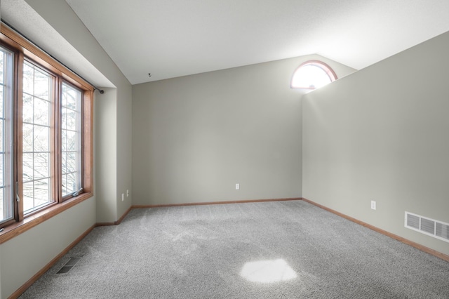 carpeted empty room featuring vaulted ceiling, visible vents, and a wealth of natural light