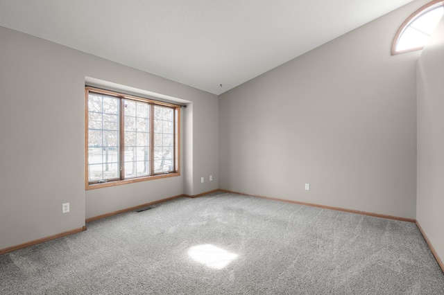 carpeted empty room with visible vents, baseboards, and vaulted ceiling