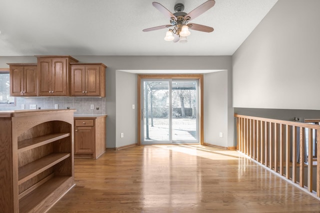 kitchen with a ceiling fan, open shelves, light countertops, light wood-type flooring, and backsplash