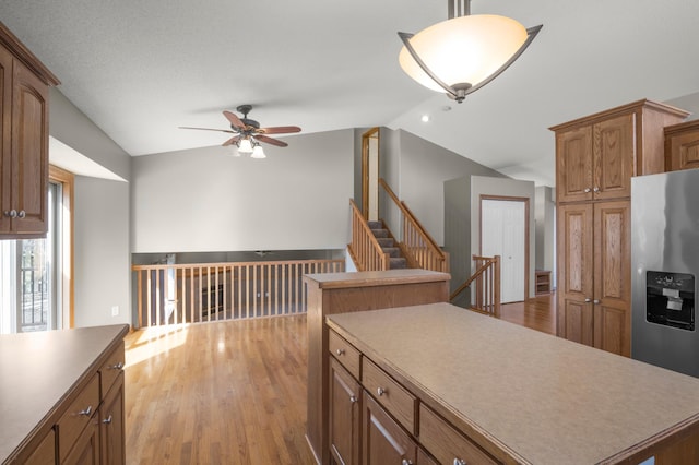 kitchen featuring vaulted ceiling, brown cabinets, light wood-style floors, stainless steel refrigerator with ice dispenser, and a ceiling fan