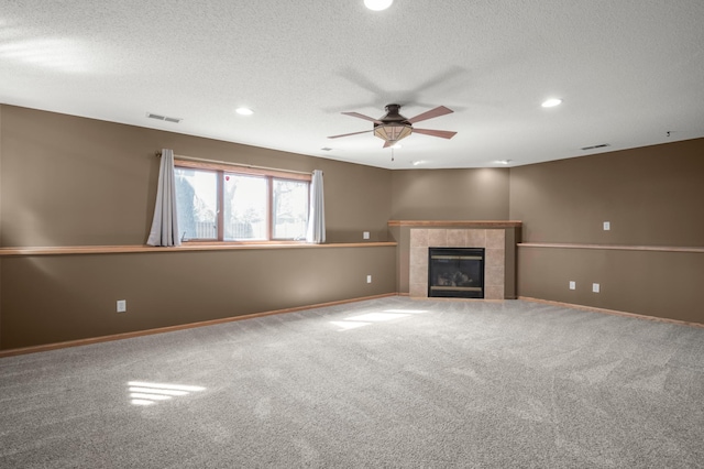 unfurnished living room featuring visible vents, a textured ceiling, carpet floors, ceiling fan, and a tile fireplace