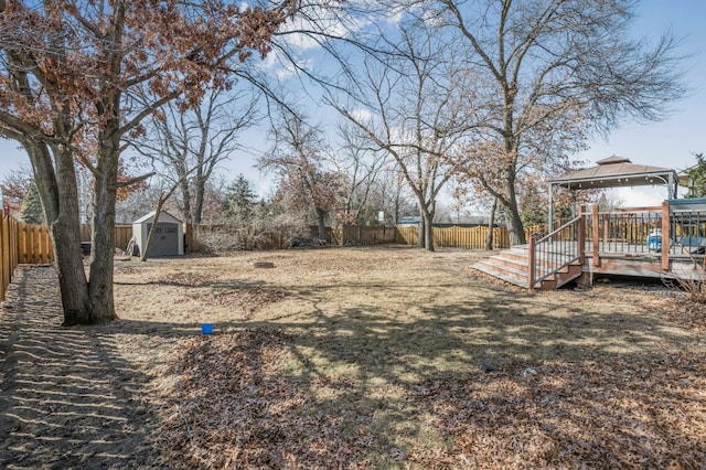 view of yard featuring a wooden deck, a gazebo, a storage shed, a fenced backyard, and an outbuilding