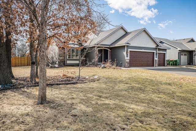 view of front of home featuring a front lawn, fence, a garage, stone siding, and driveway