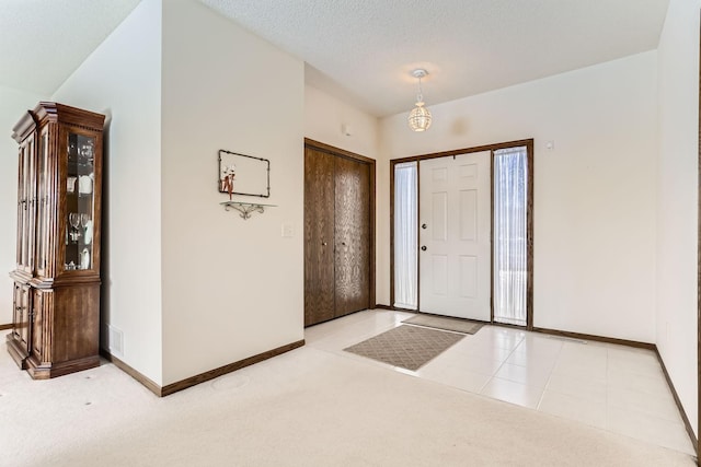 carpeted entrance foyer with tile patterned floors, visible vents, a textured ceiling, and baseboards