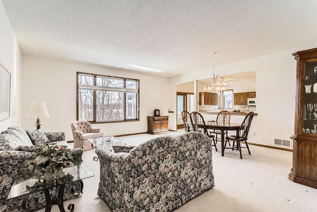 living area featuring visible vents, baseboards, light carpet, an inviting chandelier, and a textured ceiling