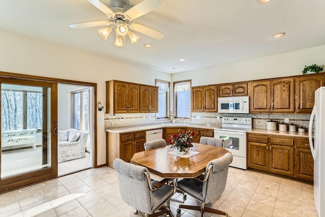 kitchen with white appliances, backsplash, brown cabinetry, and light countertops