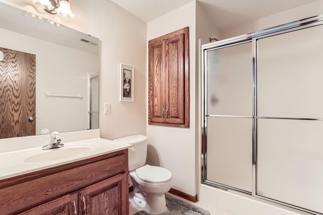 bathroom with vanity, a shower with shower door, toilet, and visible vents