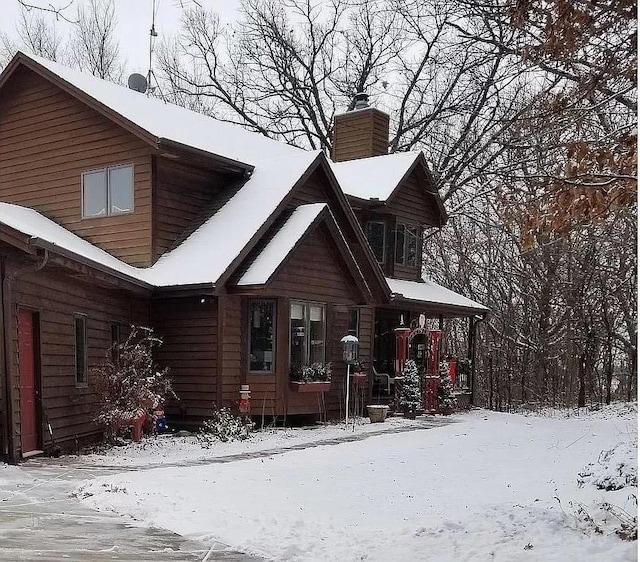 snow covered back of property featuring a chimney