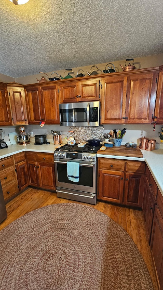 kitchen with light wood-type flooring, stainless steel appliances, brown cabinets, and a textured ceiling