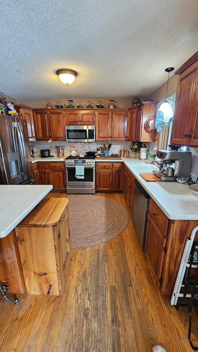 kitchen with brown cabinets, light wood-style flooring, decorative light fixtures, appliances with stainless steel finishes, and light countertops