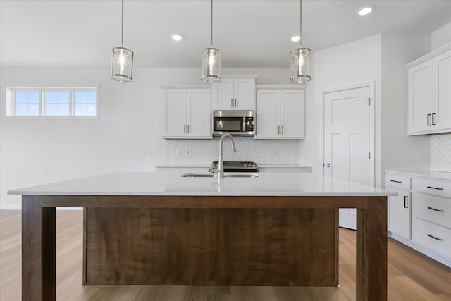 kitchen with a center island with sink, hanging light fixtures, light countertops, white cabinets, and stainless steel microwave