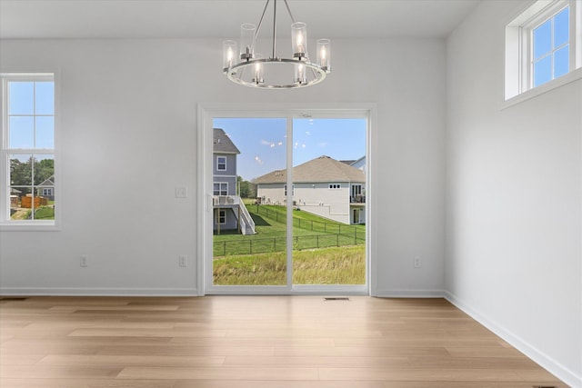 unfurnished dining area featuring baseboards, light wood finished floors, an inviting chandelier, and a healthy amount of sunlight