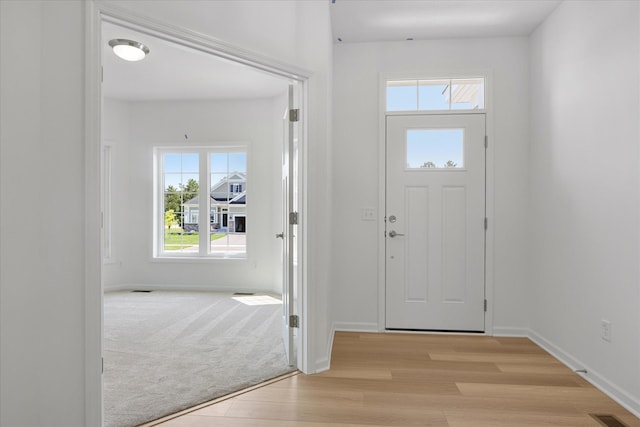 entryway featuring light carpet, visible vents, light wood-type flooring, and baseboards