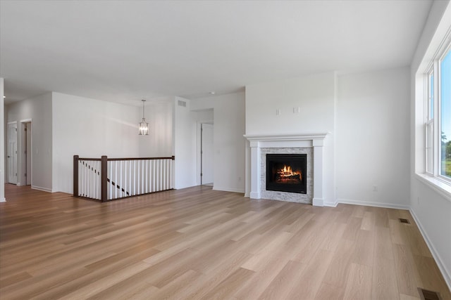 unfurnished living room featuring light wood finished floors, visible vents, baseboards, and a lit fireplace