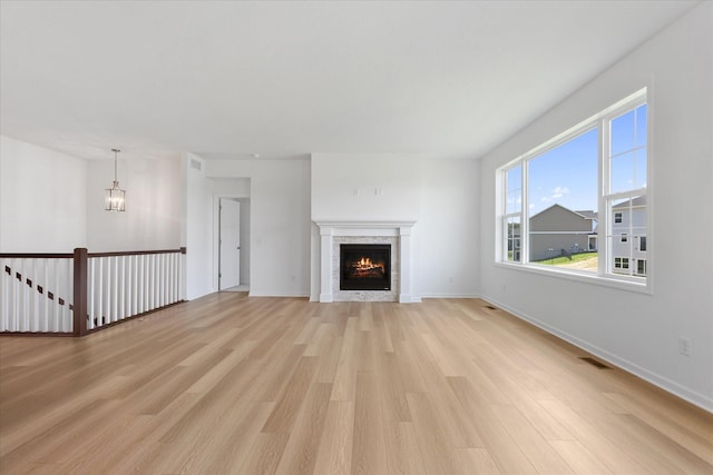 unfurnished living room with visible vents, baseboards, a lit fireplace, and light wood-style flooring