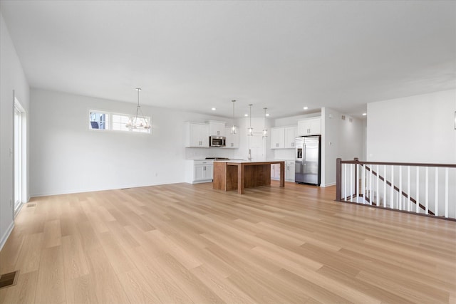 unfurnished living room featuring a chandelier, recessed lighting, light wood-style flooring, and baseboards