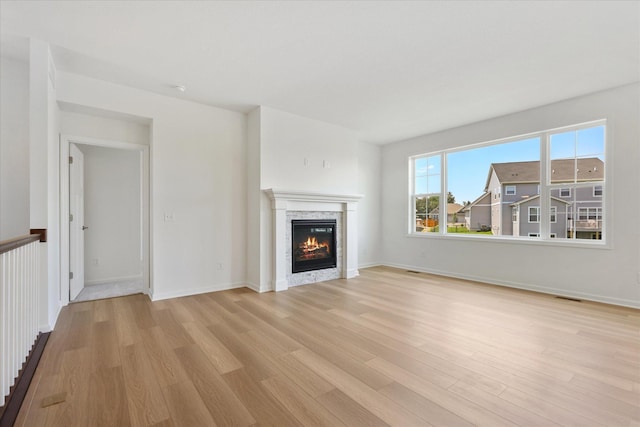 unfurnished living room with a stone fireplace, baseboards, and light wood finished floors