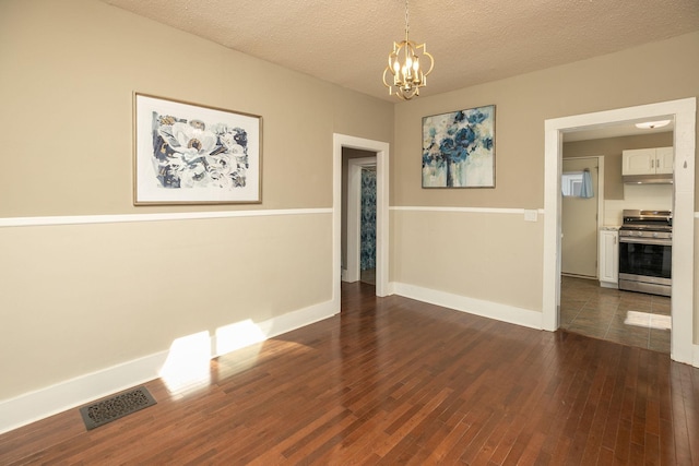 empty room with dark wood-style floors, baseboards, visible vents, an inviting chandelier, and a textured ceiling