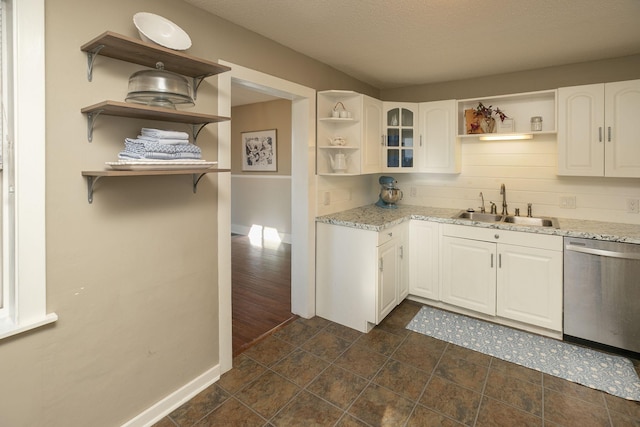 kitchen featuring stainless steel dishwasher, open shelves, light stone counters, and a sink