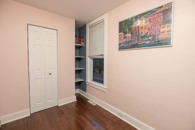 unfurnished bedroom with a closet, visible vents, dark wood-type flooring, and baseboards