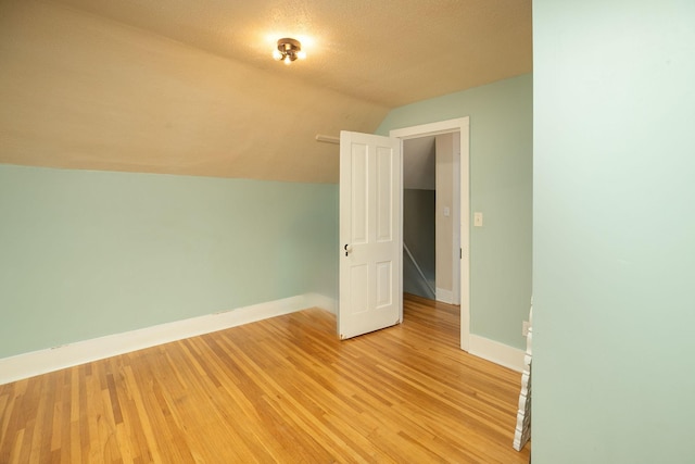 additional living space featuring lofted ceiling, baseboards, light wood-type flooring, and a textured ceiling