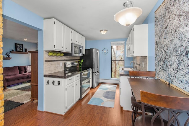 kitchen with dark countertops, appliances with stainless steel finishes, wood finished floors, white cabinetry, and a sink