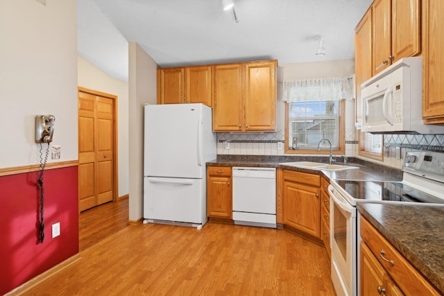 kitchen featuring white appliances, dark countertops, light wood-type flooring, and a sink