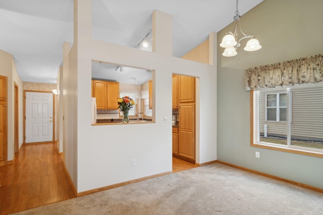 interior space with track lighting, baseboards, light colored carpet, an inviting chandelier, and high vaulted ceiling