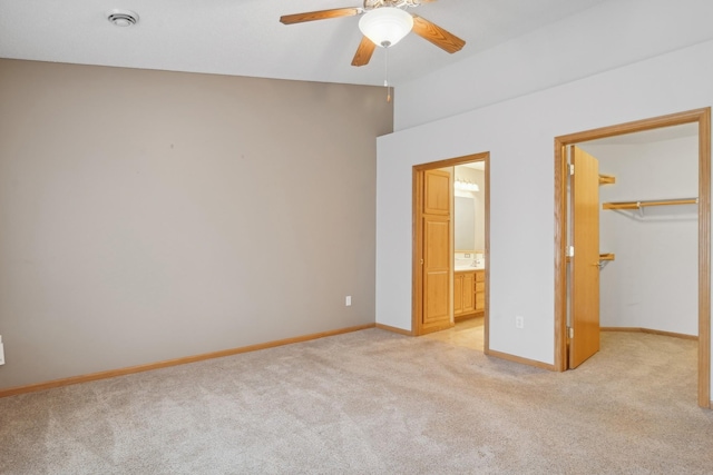 unfurnished bedroom with light carpet, a closet, connected bathroom, baseboards, and a spacious closet