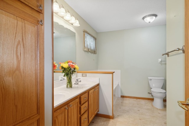 bathroom with baseboards, toilet, double vanity, a bath, and a sink