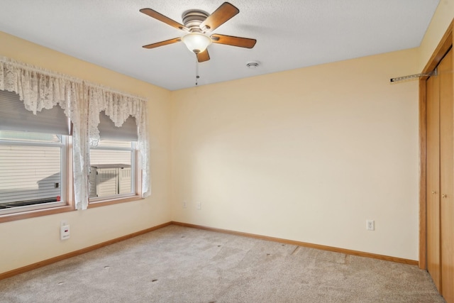 unfurnished room featuring light colored carpet, a ceiling fan, and baseboards