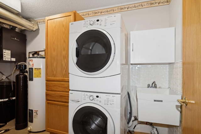 clothes washing area featuring stacked washing maching and dryer, cabinet space, water heater, a sink, and a textured ceiling