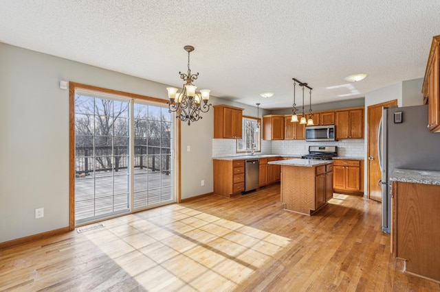 kitchen featuring a kitchen island, an inviting chandelier, stainless steel appliances, decorative backsplash, and brown cabinets