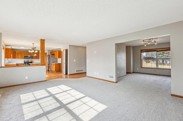 unfurnished living room featuring baseboards, visible vents, an inviting chandelier, a textured ceiling, and light colored carpet