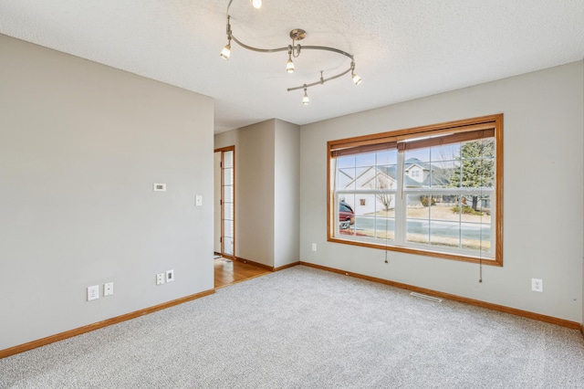 unfurnished room featuring visible vents, baseboards, carpet floors, track lighting, and a textured ceiling