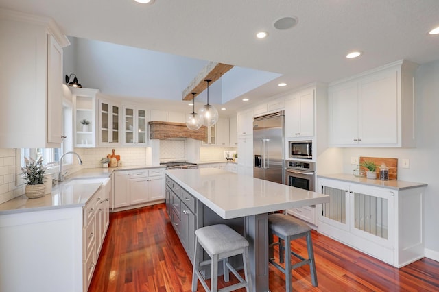 kitchen with a kitchen island, dark wood-type flooring, built in appliances, white cabinetry, and a sink